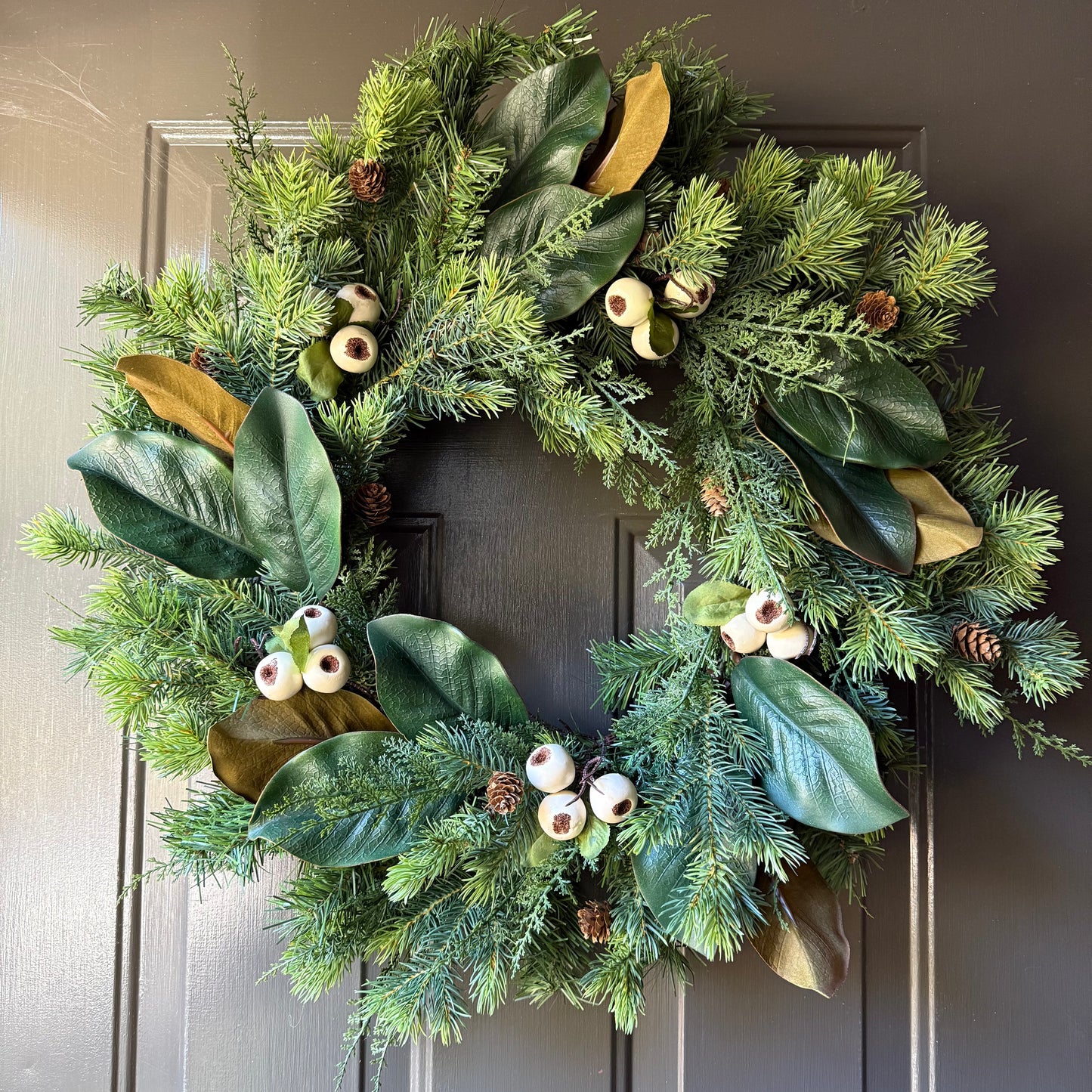 Evergreen wreath with clusters of magnolia leaves and creamy white pods/berries, and mini pinecones.