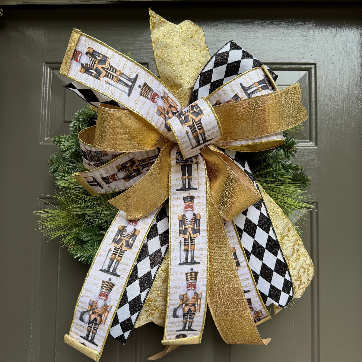 Handcrafted white nutcracker holiday bow with black-and-white diamond ribbon and gold accents, styled on a greenery wreath.