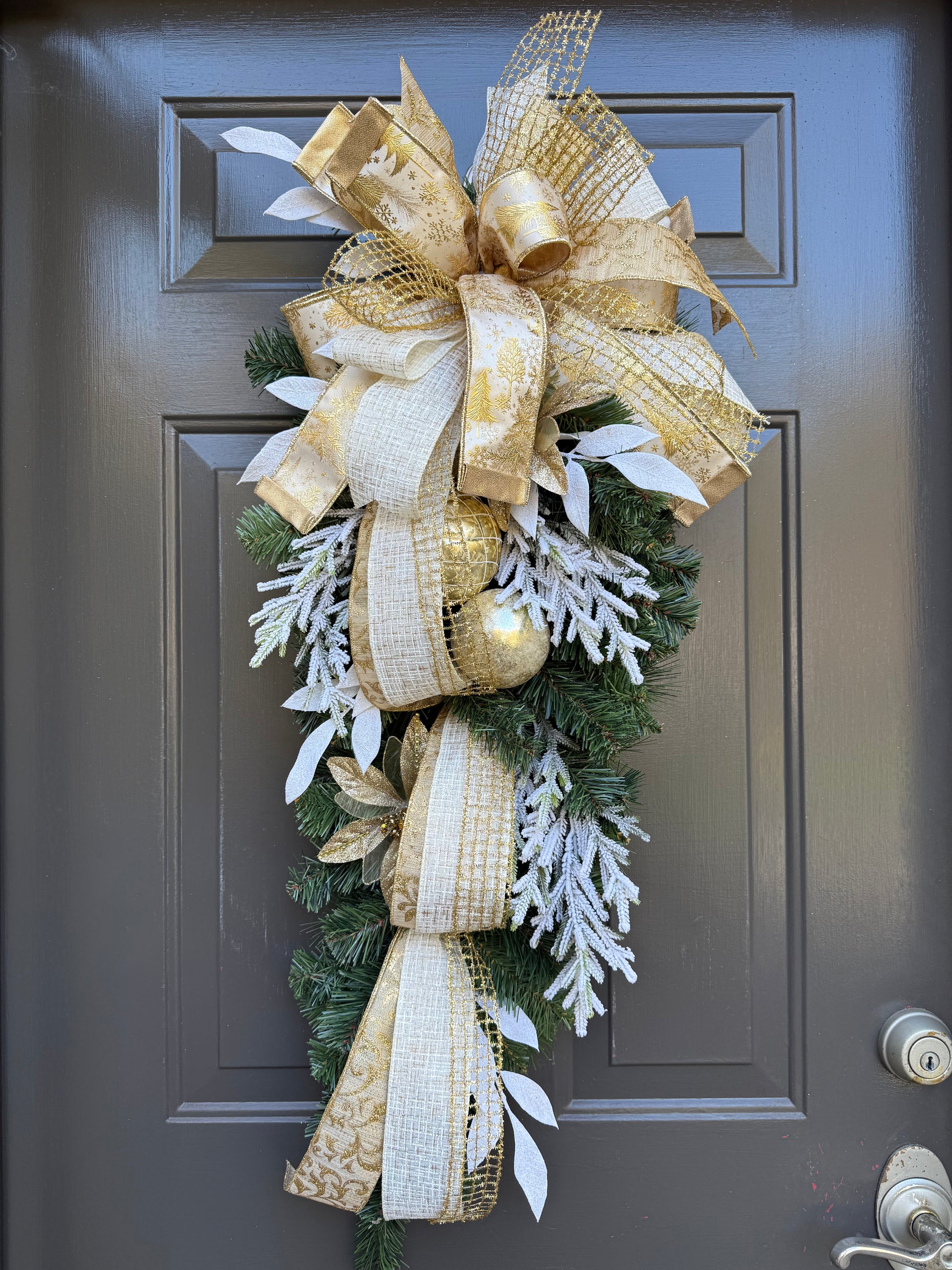 Decorative front door swag with gold and white ribbons on a door