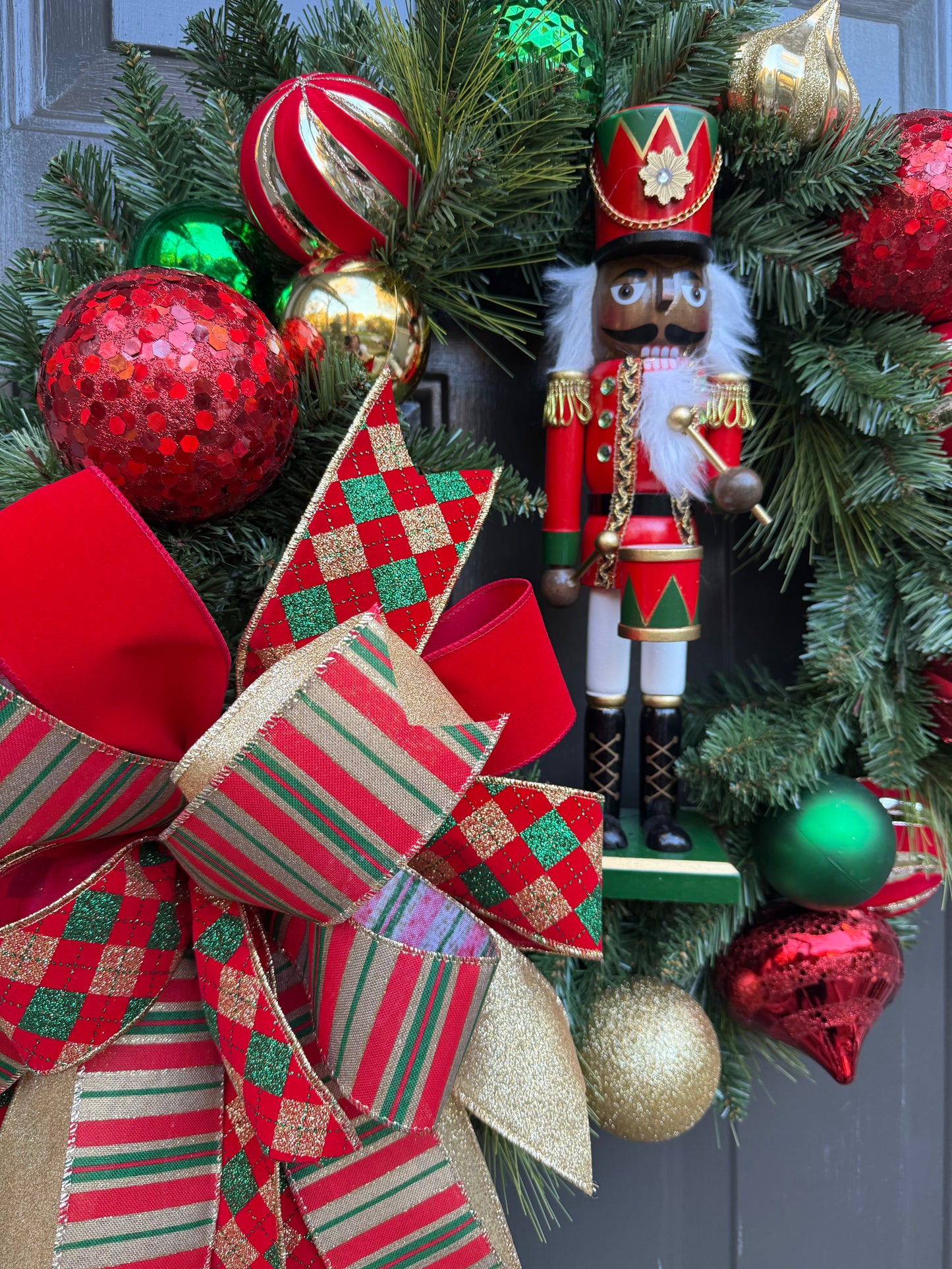 Decorative Christmas wreath with red and green ornaments and a nutcracker figure.