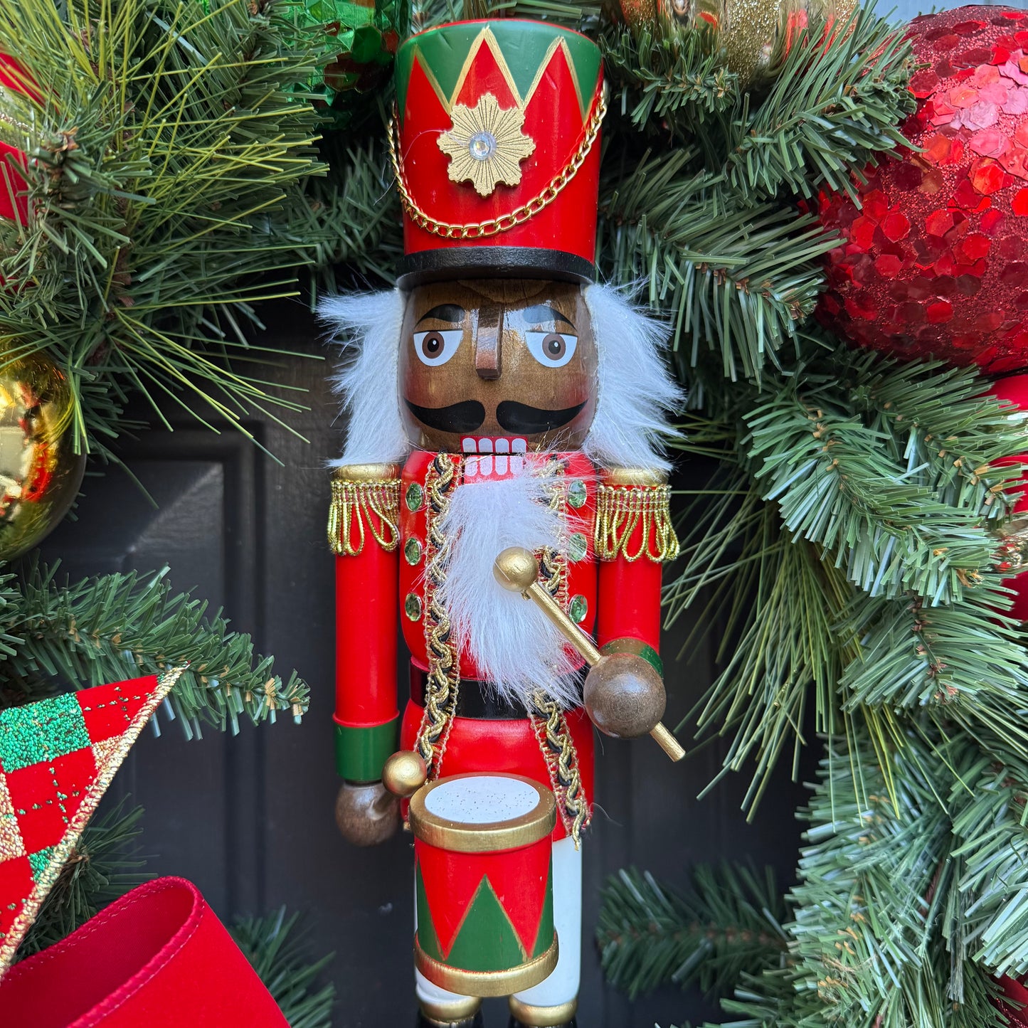 Decorative nutcracker figure with red, green, and gold colors, surrounded by Christmas wreath.