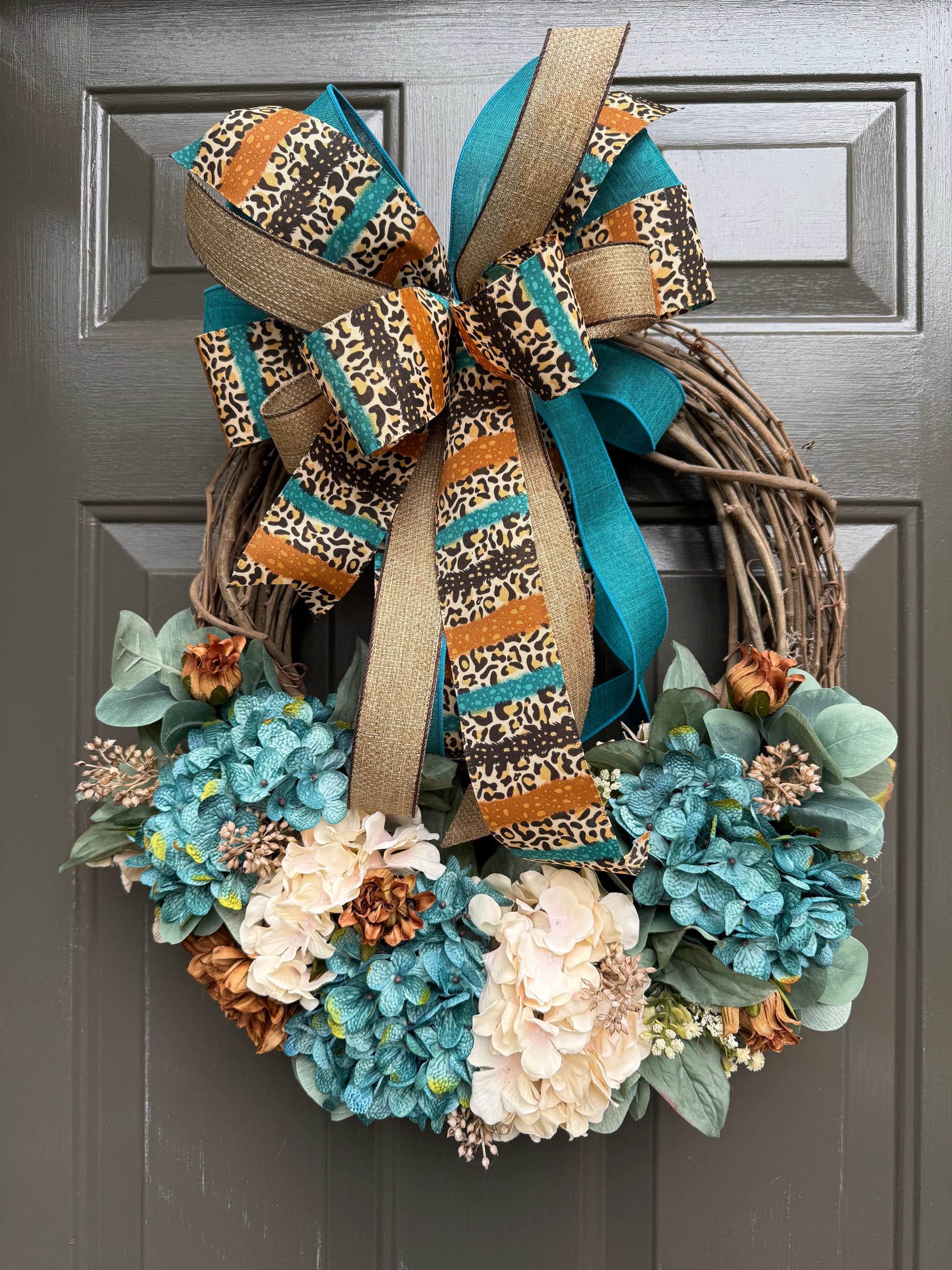 Decorative wreath with teal, white, and orange flowers and a leopard print bow.